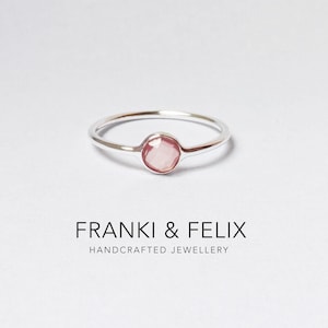 May include: A silver ring with a round, faceted, light pink gemstone. The ring is set on a white background. The text "FRANKI & FELIX HANDCRAFTED JEWELLERY" is below the ring.