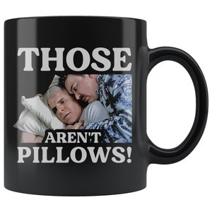 Puede incluir: Taza de café negra con un gráfico blanco de dos hombres en la cama. El texto en la taza dice "Those Aren't Pillows!"