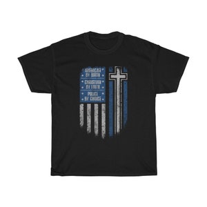 Könnte beinhalten: Schwarzes T-Shirt mit einem blau-weißen amerikanischen Flaggen-Design. Die Flagge hat eine dünne blaue Linie und ein Kreuz mit Sternen oben. Der Text auf dem Shirt lautet "American by Birth, Christian by Faith, Police by Choice."