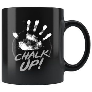 Puede incluir: Taza de café de cerámica negra con una huella de mano blanca y el texto "CHALK UP!" en una fuente blanca desgastada.