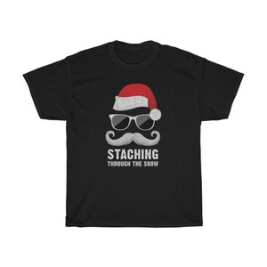 May include: Black t-shirt with a white graphic of a Santa Claus wearing sunglasses and a mustache. The text "STACHING THROUGH THE SNOW" is below the graphic.
