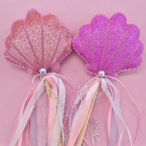 Puede incluir: Dos varitas de conchas de mar de purpurina rosa y p&uacute;rpura con cintas blancas y rosas. Las varitas son perfectas para una fiesta o un disfraz con tem&aacute;tica de sirenas.
