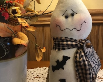 May include: A white Halloween ghost decoration with a curved head, black eyes, and a stitched mouth. It has a black and white checkered scarf and black bat cutouts. A tag reads "Spooky".