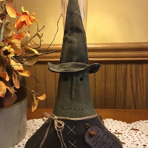 May include: A handmade Halloween witch doll with a tall, pointed hat and a dark green body. The doll has stitched facial features and a tag that reads "Witch". It is tied with twine and has a rustic, homespun appearance.