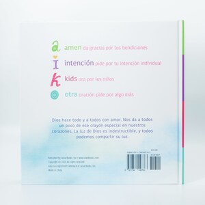 May include: A book cover with a light blue background and a colorful design. The book title is "Aiko" and the text on the back cover says "Dios hace todo y a todos con amor. Nos da a todos un poco de ese cray&oacute;n especial en nuestros corazones. La luz de Dios es indestructible, y todos podemos compartir su luz."