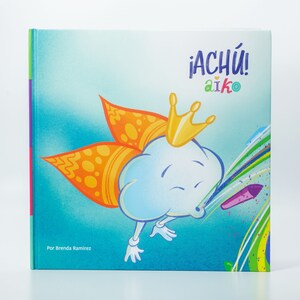 May include: A blue and yellow children's book with the title "&iexcl;ACh&Iacute;! aiko" and a cartoon cloud wearing a crown and blowing rainbow colored paint.