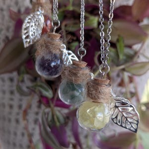 May include: Four silver chain necklaces with small glass bottles filled with different colored crystals. Each bottle has a cork stopper and a silver leaf charm.