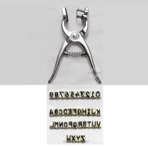 May include: A silver metal leather stamping tool with a spring and a set of interchangeable letter stamps. The letter stamps are arranged in rows and include the letters A through Z.