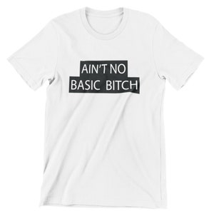 Puede incluir: Camiseta blanca con texto negro que dice "Ain't No Basic Bitch" en un cuadro.