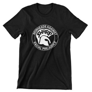 Op de afbeelding: Zwart T-shirt met een witte cirkelvormige afbeelding met de tekst "Skinheads Against Racial Prejudice" met een Spartaanse helm in de cirkel en het woord "SHARP" in hoofdletters.