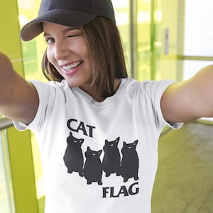 Könnte beinhalten: Ein weißes T-Shirt mit einer schwarzen Grafik von vier Katzen und dem Text "CAT FLAG".