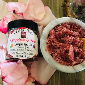 May include: A glass jar of grapefruit and rose sugar scrub with a black lid. The jar is labeled "New Dawn Elements Grapefruit & Rose Sugar Scrub Handcrafted Energize Moisturize Invigorate All Natural Skin Care Nt Wt. 4 oz".