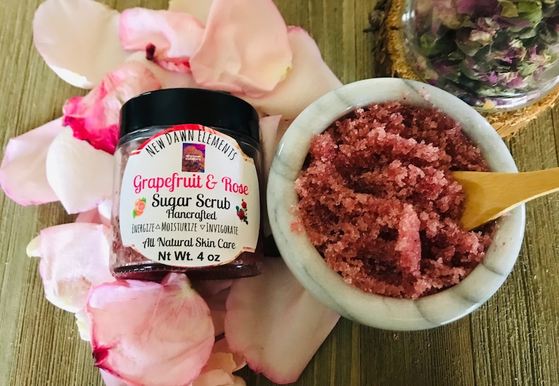 May include: A glass jar of grapefruit and rose sugar scrub with a black lid. The jar is labeled "New Dawn Elements Grapefruit & Rose Sugar Scrub Handcrafted Energize Moisturize Invigorate All Natural Skin Care Nt Wt. 4 oz".