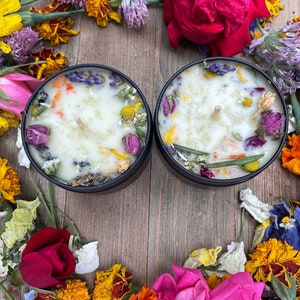 May include: Two black candle jars filled with white wax and dried flowers. The jars are surrounded by a variety of dried flowers, including roses, marigolds, and lavender.