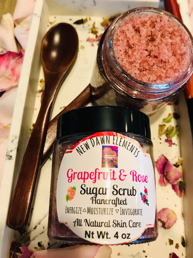 May include: A glass jar of pink grapefruit and rose sugar scrub with a black lid. The label reads "NEW DAWN ELEMENTS Grapefruit & Rose Sugar Scrub Hancrafted ENERGIZE MOISTURIZE INVIGORATE All Natural Skin Care Nt Wt. 4 oz".