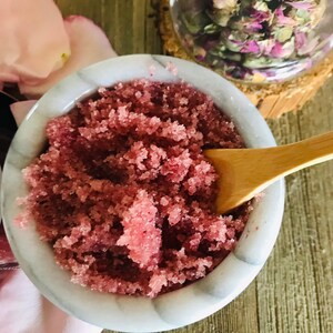May include: A close-up of a white bowl filled with pink sugar scrub. The scrub is made with rose petals and is perfect for exfoliating the skin.