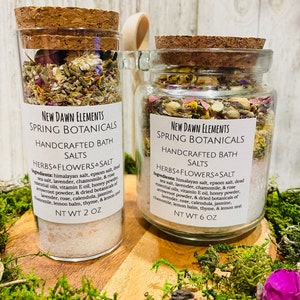 Puede incluir: Dos frascos de vidrio llenos de hierbas y flores secas, etiquetados como "New Dawn Elements Spring Botanicals Handcrafted Bath Salts Herbs & Flowers & Salt". El frasco más pequeño está etiquetado como "NT WT 2 OZ" y el más grande como "NT WT 6 OZ".