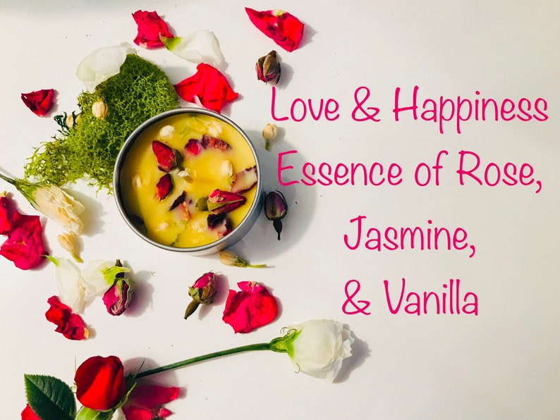 Op de afbeelding: Een witte kaars met gedroogde rozenblaadjes en andere botanische elementen in een zilveren blik. De kaars is omringd door rozenblaadjes en andere bloemen. De tekst "Love & Happiness Essence of Rose, Jasmine, & Vanilla" is in roze op een witte achtergrond geschreven.