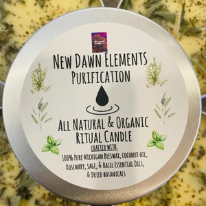 Op de afbeelding: Een zilveren blikje met een kaars met een gele wax bovenkant en gedroogde kruiden. Het etiket luidt "New Dawn Elements Purification All Natural & Organic Ritual Candle Crafted With: 100% Pure Michigan Beeswax, Coconut Oil, Rosemary, Sage, & Basil Essential Oils, & Dried Botanicals"