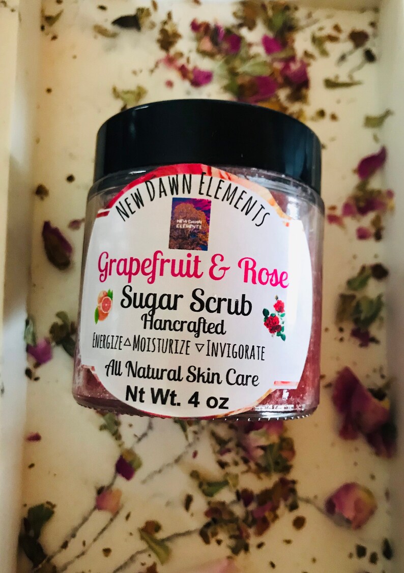 May include: A glass jar of grapefruit and rose sugar scrub with a black lid. The label reads "New Dawn Elements Grapefruit & Rose Sugar Scrub Hancrafted Energize Moisturize Invigorate All Natural Skin Care Nt Wt. 4 oz".