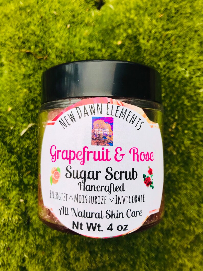 May include: A glass jar with a black lid containing a pink and white sugar scrub. The label reads "NEW DAWN ELEMENTS Grapefruit & Rose Sugar Scrub Hancrafted ENERGIZE MOISTURIZE INVIGORATE All Natural Skin Care Nt Wt. 4 oz".