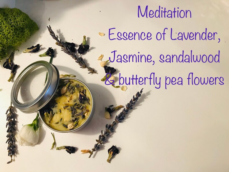 Op de afbeelding: Een klein blikje met een kaars en een doorzichtig deksel. De kaars is wit met lavendel, jasmijn en sandelhoutbloemen. De tekst op het etiket luidt "Meditation Essence of Lavender, Jasmine, sandalwood & butterfly pea flowers".