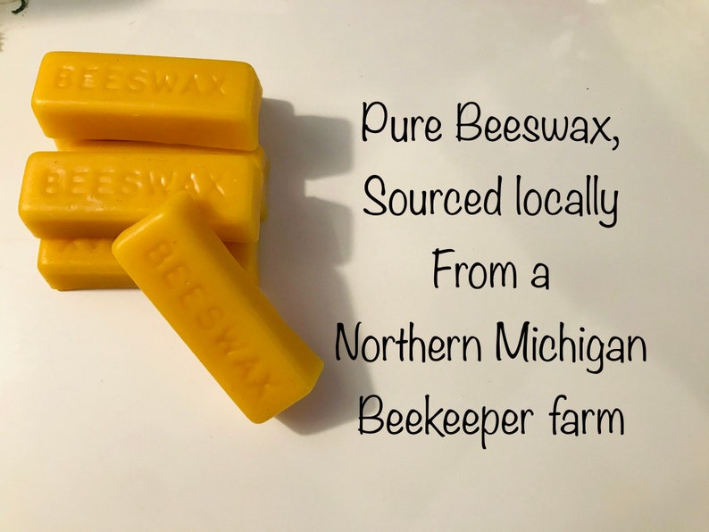 Op de afbeelding: Een stapel van vijf gele bijenwasstaven, elk met het label "BEESWAX". De tekst "Pure Beeswax, Sourced locally From a Northern Michigan Beekeeper farm" staat onder de staven.