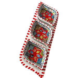 May include: A set of three small, white ceramic dishes with a red and white dotted border. Each dish has a floral design in red, yellow, blue, and black. The dishes are arranged on a rectangular tray.