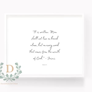Op de afbeelding: Een witte ingelijste print met een zwart-wit tekstcitaat uit de Bijbel: "Er staat geschreven: De mens zal niet van brood alleen leven, maar van elk woord dat uit de mond van God komt." - Jezus. Mattheüs 4:4