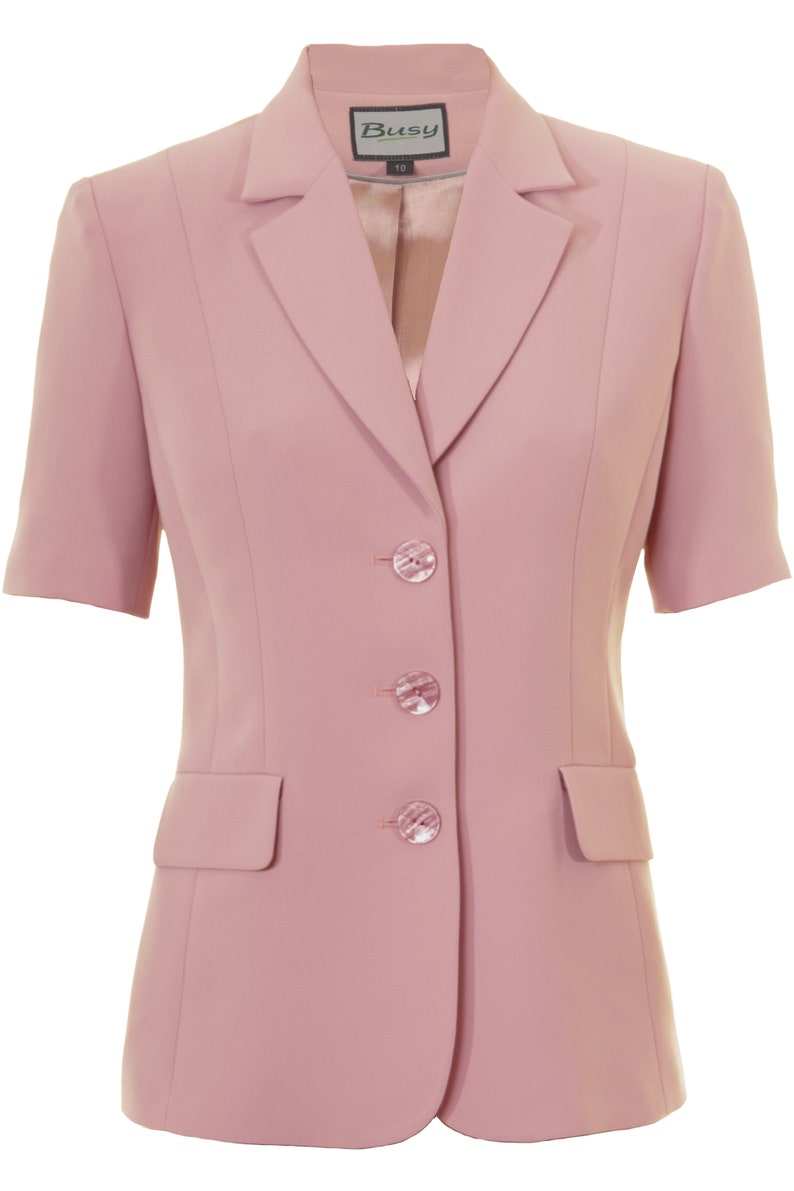 May include: A pink short-sleeved blazer with a notched collar and three buttons. The blazer has a pocket on the left side and a label that says "Busy" on the collar.