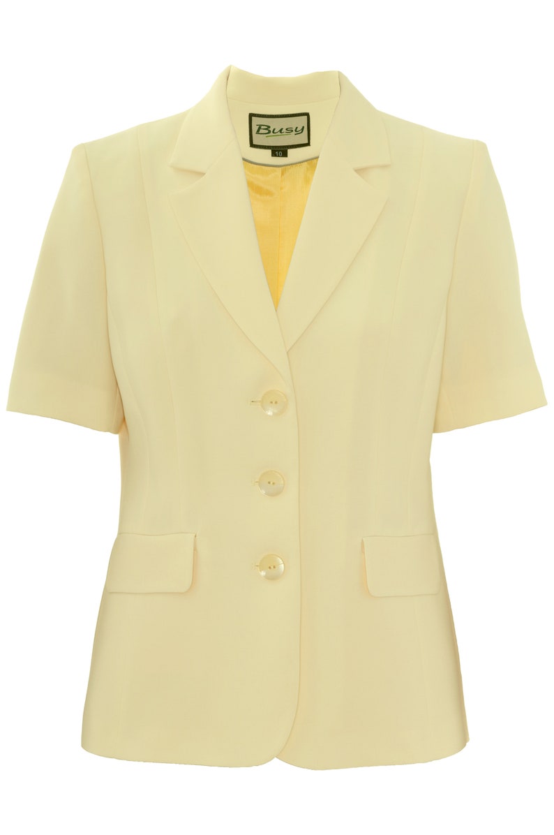 May include: A pale yellow short-sleeved blazer with four buttons and a pocket on the left side. The blazer has a label that says "Busy" on it.