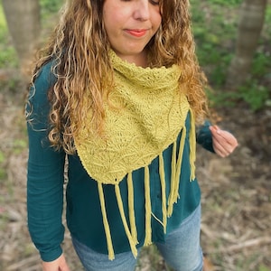 Puede incluir: Una mujer con una camisa verde azulada y una chalina amarilla de ganchillo con flecos. La chalina tiene un patrón de hojas.
