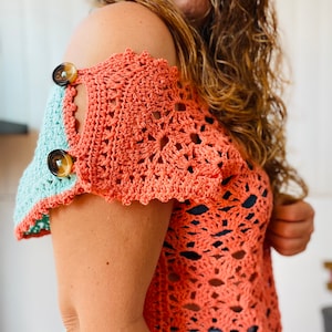 Può includere: Un top all'uncinetto in corallo e turchese. Il top ha un design a uncinetto con un bordo a scalare e presenta due grandi bottoni sulla spalla.