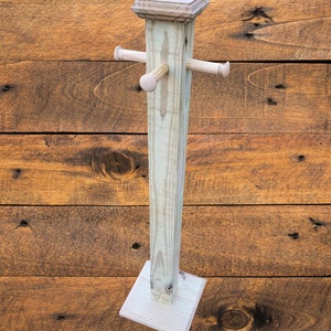 May include: A wooden towel rack with a square base and four wooden dowels. The rack is made of natural wood and has a rustic look.
