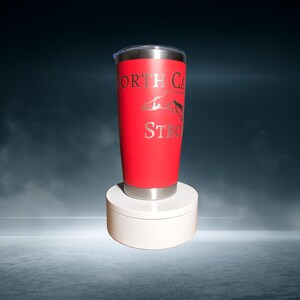 May include: A red stainless steel tumbler with a silver lid and a silver outline of the state of North Carolina with the words "North Carolina Strong" printed on it.