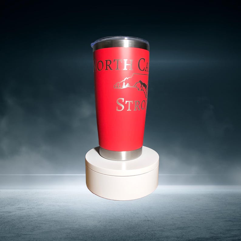 May include: A red stainless steel tumbler with a silver lid and a silver outline of the state of North Carolina with the words "North Carolina Strong" printed on it.