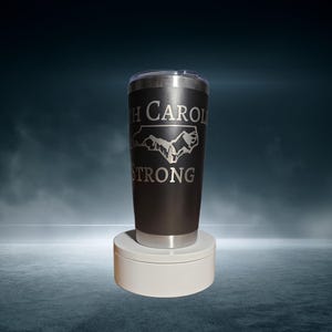 May include: A black stainless steel tumbler with a white outline of the state of North Carolina and the text "North Carolina Strong".