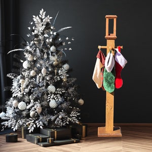 May include: A decorated Christmas tree with silver and white ornaments and a wooden stocking holder. The holder has four Christmas stockings in red, green, and white. Several wrapped gifts are at the base of the tree.