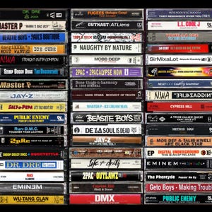 Puede incluir: Una colección de cintas de cassette vintage con títulos de álbumes y nombres de artistas como Dr. Dre, Beastie Boys y 2Pac. Las cintas están apiladas en filas, mostrando una variedad de música hip-hop y rap de los años 90 y principios de los 2000.