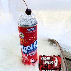 May include: A stainless steel tumbler featuring a red and white Kool-Aid Cherry design. The tumbler has a cherry on top and ice cubes inside. The tumbler is on a white fluffy surface with a red and white logo that says "Voorhees Tumblers".