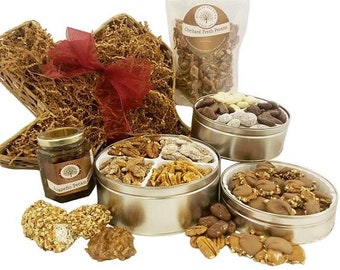 May include: A gift basket filled with pecans in various forms, including a jar of candied pecans, a bag of pecans, and three round tins of pecans. The tins are filled with different types of pecans, including chocolate-covered pecans, candied pecans, and plain pecans. The basket is decorated with a red bow and brown shredded paper.
