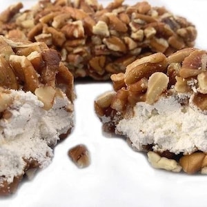 May include: Two pecan-covered treats with a white filling, broken open to reveal the filling. The treats are on a white surface.