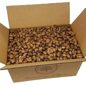 May include: A cardboard box filled with pecan shells. The box is open and the pecans are visible. The box has the text "MillianPecan.com - San Saba, TX" printed on the bottom.