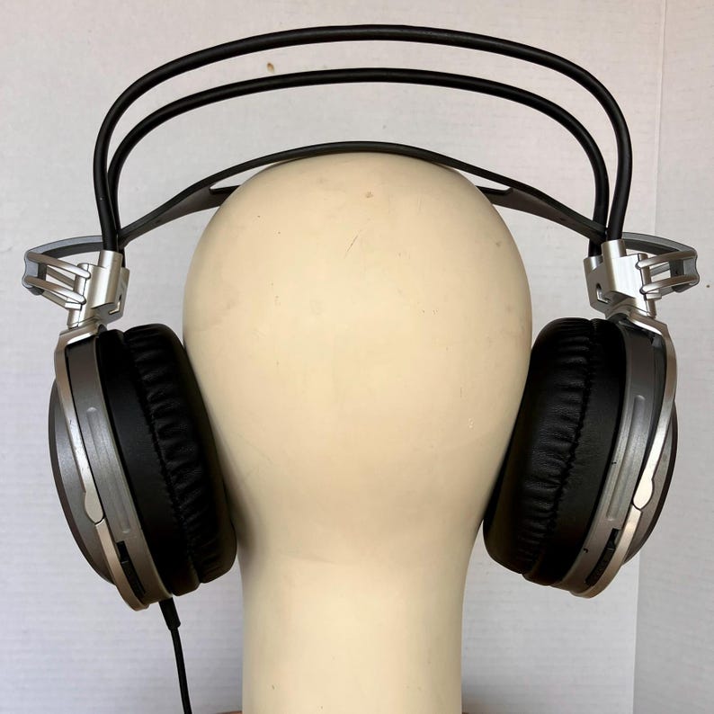May include: Silver and black over-ear headphones with a padded headband and earcups. The headphones have a sleek design with silver accents and a black cable. The earcups are round and have a soft, black cushion for comfort.