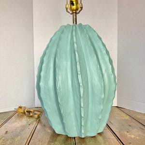 May include: A light blue ceramic table lamp with a cactus-like design. The lamp has a textured surface with vertical ridges and a brass-colored lamp holder. The lamp is approximately 18 inches tall.