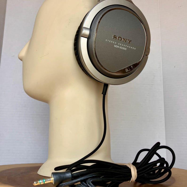 May include: Silver and gray Sony MDR-XD300 stereo headphones with a black cord and gold-tipped plug. The headphones are resting on a mannequin head. The Sony logo and model number are visible on the ear cup.
