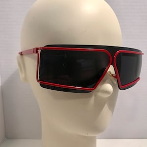May include: Red and black sunglasses with a geometric frame. The sunglasses have a wide, rectangular shape and are made of plastic.