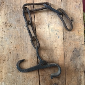May include: A rusty metal chain with a hook on one end and a loop on the other. The chain is hanging on a wooden surface.