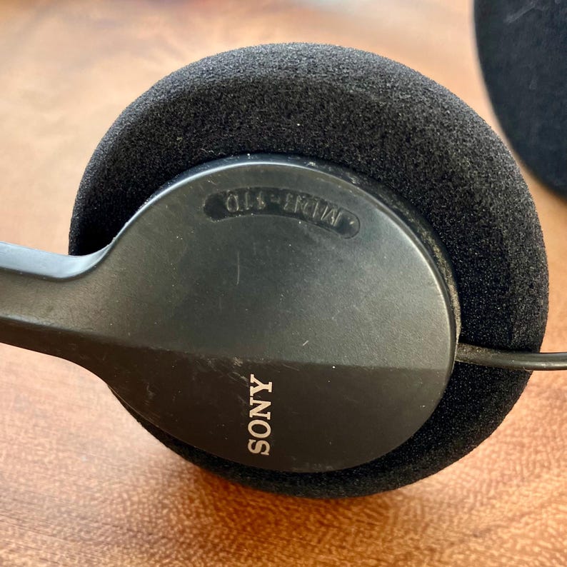 May include: Black Sony headphones with a round, cushioned ear cup. The ear cup has the word "SONY" printed in white. The ear cup is surrounded by a black foam cushion. The model number "MDR-110" is printed on the ear cup.