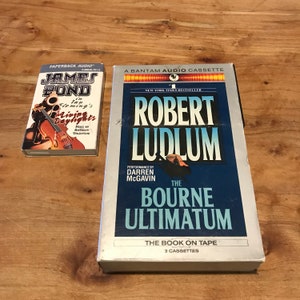 May include: Two audio cassette tapes. The first is a James Bond audio cassette with the title "In Ian Fleming's Living Daylights". The second is a Robert Ludlum audio cassette with the title "The Bourne Ultimatum".